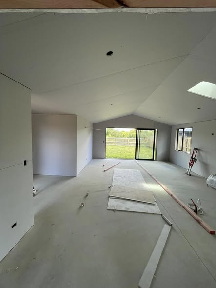 Vaulted ceiling, two-pitch roof line, fresh gib stopping above and a sliding door view through to a rural Waikato section