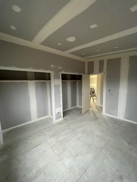 Bedroom mid-build, gib walls stopped and ready for paint, two windows looking out to grass and fence line